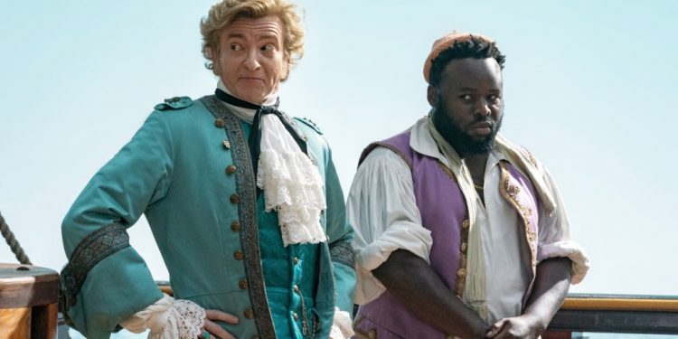 Foppish "gentleman pirate" Stede (Rhys Darby), left, with his crew member Oluwande (Samson Kayo), right, stand on the deck of a ship.