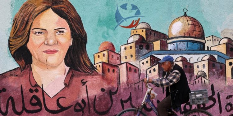 A Palestinian man rides his bicycle in front of a mural painted by an artist in honour of slain veteran Al-Jazeera journalist Shireen Abu Akleh, in Gaza City on May 13, 2022. - Abu Akleh, who was shot dead on May 11, 2022 while covering a raid in the Israeli-occupied West Bank, was among Arab media's most prominent figures and widely hailed for her bravery and professionalism.