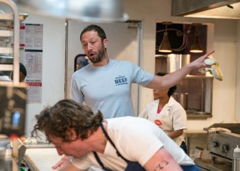 Ebon Moss-Bacharach as Richie. He's wearing a T-shirt that says The Original Beef of Chicagoland and is yelling at Carmy, who's leaning over and scrubbing something. Richie is pointing to something off-camera.