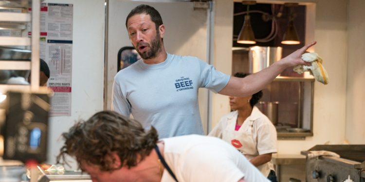 Ebon Moss-Bacharach as Richie. He's wearing a T-shirt that says The Original Beef of Chicagoland and is yelling at Carmy, who's leaning over and scrubbing something. Richie is pointing to something off-camera.